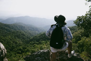 Dağın tepesinde kadın yürüyüşçü. Kolları dağın tepesinde gezen başarılı genç bir kadın zaferin tadını çıkarıyor. Gezgin dünyayı keşfediyor. Sırt çantalı yürüyüşçüler dinleniyor. Spor ve başarı konsepti.