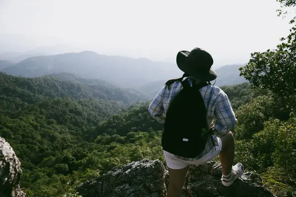 Dağın tepesinde kadın yürüyüşçü. Kolları dağın tepesinde gezen başarılı genç bir kadın zaferin tadını çıkarıyor. Gezgin dünyayı keşfediyor. Sırt çantalı yürüyüşçüler dinleniyor. Spor ve başarı konsepti.