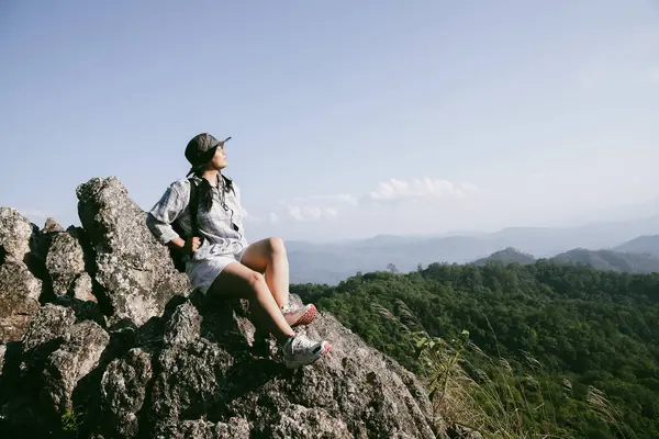 Dağın tepesinde kadın yürüyüşçü. Kolları dağın tepesinde gezen başarılı genç bir kadın zaferin tadını çıkarıyor. Gezgin dünyayı keşfediyor. Sırt çantalı yürüyüşçüler dinleniyor. Spor ve başarı konsepti.