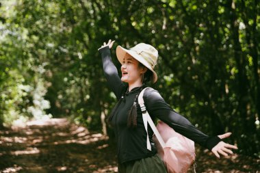 Sırt çantalı genç bir gezgin ulusal parkta ya da ormanda yürüyor. Doğada eğlence sporu. Kadın çantası, ormanda yürüyüş için el sallıyor. Ormanda macera. Sırt çantasıyla yürüyüş