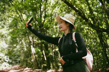 Sırt çantalı genç bir gezgin ulusal parkta ya da ormanda yürüyor. Doğada eğlence sporu. Kadın çantası, ormanda yürüyüş için el sallıyor. Ormanda macera. Sırt çantasıyla yürüyüş