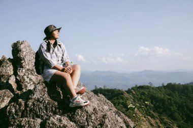 Dağın tepesinde kadın yürüyüşçü. Kolları dağın tepesinde gezen başarılı genç bir kadın zaferin tadını çıkarıyor. Gezgin dünyayı keşfediyor. Sırt çantalı yürüyüşçüler dinleniyor. Spor ve başarı konsepti.