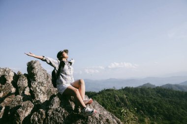 Dağın tepesinde kadın yürüyüşçü. Kolları dağın tepesinde gezen başarılı genç bir kadın zaferin tadını çıkarıyor. Gezgin dünyayı keşfediyor. Sırt çantalı yürüyüşçüler dinleniyor. Spor ve başarı konsepti.