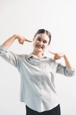 Asyalı bir kadın seviniyor, mutlu görünüyor, şampiyon, yumruk sallıyor, beyaz arka planda duruyor. Genç bir kadının yüzünde mutlu, pozitif bir ifade vardı. Parlak bir gülümsemeyle vurgulanmıştı..