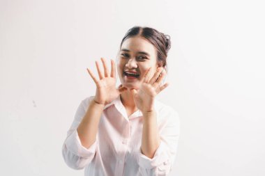 Asyalı bir kadın seviniyor, mutlu görünüyor, şampiyon, yumruk sallıyor, beyaz arka planda duruyor. Genç bir kadının yüzünde mutlu, pozitif bir ifade vardı. Parlak bir gülümsemeyle vurgulanmıştı..