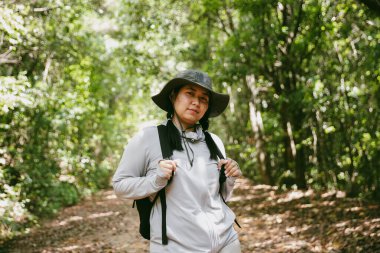 Sırt çantalı genç bir gezgin ulusal parkta ya da ormanda yürüyor. Doğada eğlence sporu. Kadın çantası, ormanda yürüyüş için el sallıyor. Ormanda macera. Sırt çantasıyla yürüyüş