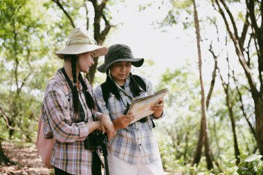 Sırt çantalı iki bayan arkadaş birlikte kırda yürüyüş yapıyorlar. Asyalı arkadaş kız sırt çantalı arkadaş ormanda birlikte seyahat eder. Yürüyüş yaparken mutlu ve güneşli bir gün..