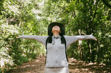 Sırt çantalı genç bir gezgin ulusal parkta ya da ormanda yürüyor. Doğada eğlence sporu. Kadın çantası, ormanda yürüyüş için el sallıyor. Ormanda macera. Sırt çantasıyla yürüyüş