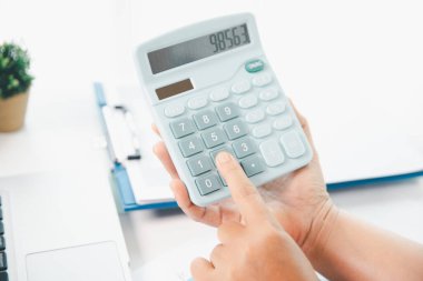 Ofisteki finans raporunu hesaplamak için hesap makinesi kullanan bir muhasebeci. işletme finansmanı, mali belgeleri düzenleyerek vergi hesaplama, gelir yatırımlarını takip etme, elle hesaplama.