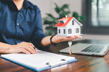 Kadın eli küçük minyatür bir oyuncak evi tutuyor, kendi emlak konseptine taşınma hayalini sembolize eden kadın emlak yatırımını, ipotek planlama, güvenli bir gelecek sigortasını temsil ediyor..