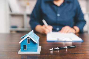 Masanın yanına yerleştirilen ev modeli madeni paraların yanı sıra, evrak işleri de gayrimenkul yatırımını, emlak değerini, mali planlama, mortgage seçeneklerini, emlak piyasasındaki pazar analizini simgeler..