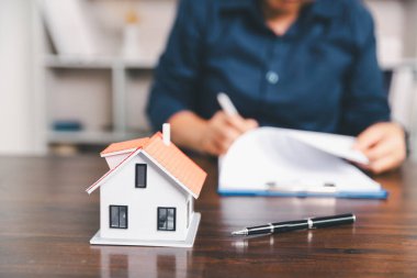 Masanın yanına yerleştirilen ev modeli madeni paraların yanı sıra, evrak işleri de gayrimenkul yatırımını, emlak değerini, mali planlama, mortgage seçeneklerini, emlak piyasasındaki pazar analizini simgeler..