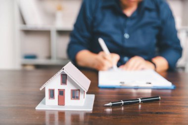 Masanın yanına yerleştirilen ev modeli madeni paraların yanı sıra, evrak işleri de gayrimenkul yatırımını, emlak değerini, mali planlama, mortgage seçeneklerini, emlak piyasasındaki pazar analizini simgeler..