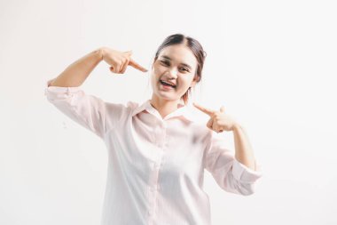 Asyalı bir kadın seviniyor, mutlu görünüyor, şampiyon, yumruk sallıyor, beyaz arka planda duruyor. Genç bir kadının yüzünde mutlu, pozitif bir ifade vardı. Parlak bir gülümsemeyle vurgulanmıştı..