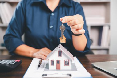 Kadın eli küçük minyatür bir oyuncak evi tutuyor, kendi emlak konseptine taşınma hayalini sembolize eden kadın emlak yatırımını, ipotek planlama, güvenli bir gelecek sigortasını temsil ediyor..