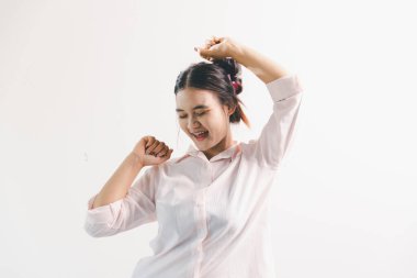 Asyalı bir kadın seviniyor, mutlu görünüyor, şampiyon, yumruk sallıyor, beyaz arka planda duruyor. Genç bir kadının yüzünde mutlu, pozitif bir ifade vardı. Parlak bir gülümsemeyle vurgulanmıştı..