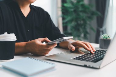 Yakın çekim sahnesinde, masada oturan bir kadın akıllı bir telefon tutuyor, modern e-randevu hizmetleri ve sosyal medyada mobil bir uygulama ile vakit geçiriyor, dijital kullanım kablosuz kavramını gösteriyor.