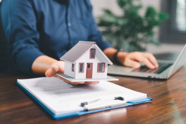 Kadın eli küçük minyatür bir oyuncak evi tutuyor, kendi emlak konseptine taşınma hayalini sembolize eden kadın emlak yatırımını, ipotek planlama, güvenli bir gelecek sigortasını temsil ediyor..