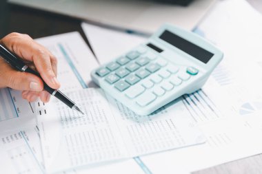 Denetçi, iş dünyası için ayrıntılı bir mali rapor hazırlamada muhasebe, denetim ve finans kavramını temsil eden bir hesap makinesi kullanarak mali beyanat ve bilançoyu masasında gözden geçirir..