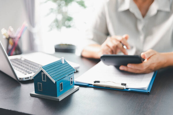 Агент по недвижимости соглашается купить дом для клиентов агентского офиса. Модель дома, агент по недвижимости, клиент обсуждает контракт на покупку дома, страхование, кредитный опыт недвижимости. Концепция соглашения.