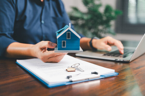 Женщина держит в руках маленький миниатюрный домик игрушки, символизирующий женскую мечту о переезде в свою собственную концепцию дома-недвижимости представляет собой инвестиции в недвижимость, ипотечное планирование, страхование безопасного будущего.