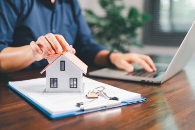 Kadın eli küçük minyatür bir oyuncak evi tutuyor, kendi emlak konseptine taşınma hayalini sembolize eden kadın emlak yatırımını, ipotek planlama, güvenli bir gelecek sigortasını temsil ediyor..