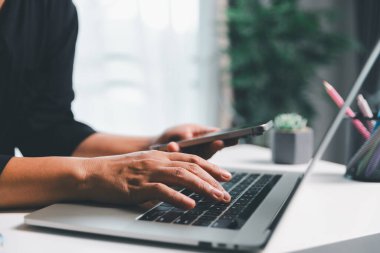 Yakın çekim sahnesinde, masada oturan bir kadın akıllı bir telefon tutuyor, modern e-randevu hizmetleri ve sosyal medyada mobil bir uygulama ile vakit geçiriyor, dijital kullanım kablosuz kavramını gösteriyor.