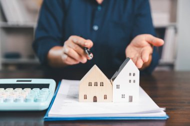 Masanın yanına yerleştirilen ev modeli madeni paraların yanı sıra, evrak işleri de gayrimenkul yatırımını, emlak değerini, mali planlama, mortgage seçeneklerini, emlak piyasasındaki pazar analizini simgeler..