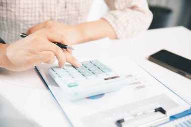 Ofisteki finans raporunu hesaplamak için hesap makinesi kullanan bir muhasebeci. işletme finansmanı, mali belgeleri düzenleyerek vergi hesaplama, gelir yatırımlarını takip etme, elle hesaplama.