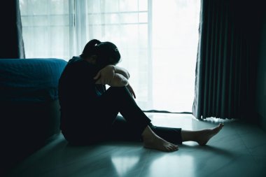 Üzgün bir kadın karanlık bir odada yerde oturuyor. Başı pencerenin yanında dinleniyor. Depresyon, stres, endişe, yalnızlık, akıl sağlığı sorunu, duygusal mücadele ve psikolojik sorun kavramı.