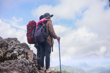 Sırt çantalarıyla dağ zirvesinde birlikte duran iki yürüyüşçü, manzara manzarasını kucaklıyor ve eğleniyor, arkadaşlığın sembolü, sevgi, destek, birlik, beraberlik, macera ve açık hava yaşam tarzı..