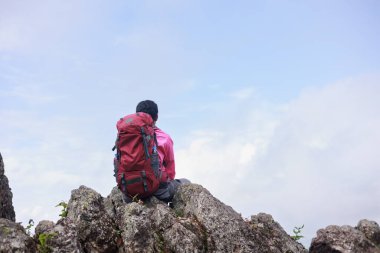 Sırt çantalı gezgin kayalık dağ zirvesinde oturmuş gökyüzüne bakıyor, maceranın, özgürlüğün, yalnızlığın, ilhamın, keşfin, doğa yaşam tarzının ve kendini keşfetmenin sembolü..