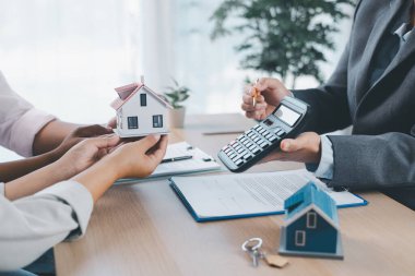 Emlak acentesinin hesap makinesi ve kontrat evraklarıyla müşteriye ev modelini teslim etmesi, ipotek kredisi konsepti, ev sahipliği, emlak yatırımı ve konut anlaşması.