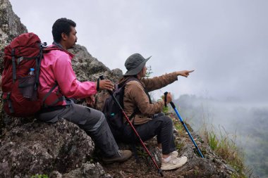 Sırt çantalı iki yürüyüşçü ve kayalık dağda dinlenen yürüyüş direkleri, ileri bakan kadın, takım çalışması, macera, keşif, açık hava yaşam tarzı ve doğada seyahat ilhamının sembolü..