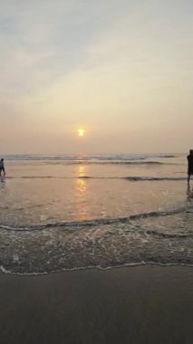 Kumsalda güzel sisli bir gün batımı. Dalgalar ve kara kumlarla.