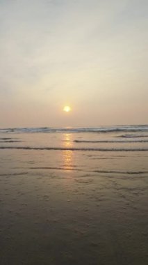 Kumsalda güzel sisli bir gün batımı. Dalgalar ve kara kumlarla.