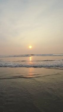 Kumsalda güzel sisli bir gün batımı. Dalgalar ve kara kumlarla.