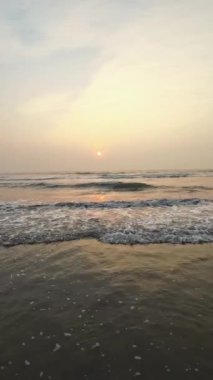 Kumsalda güzel sisli bir gün batımı. Dalgalar ve kara kumlarla.