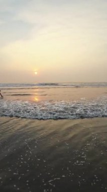 Kumsalda güzel sisli bir gün batımı. Dalgalar ve kara kumlarla.