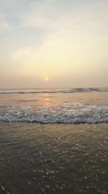 Kumsalda güzel sisli bir gün batımı. Dalgalar ve kara kumlarla.