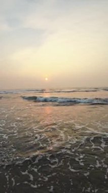 Kumsalda güzel sisli bir gün batımı. Dalgalar ve kara kumlarla.