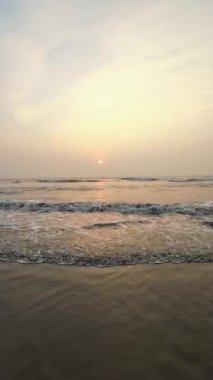 Kumsalda güzel sisli bir gün batımı. Dalgalar ve kara kumlarla.