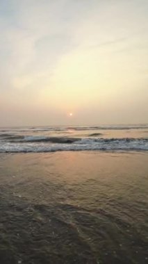 Kumsalda güzel sisli bir gün batımı. Dalgalar ve kara kumlarla.