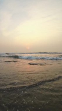 Kumsalda güzel sisli bir gün batımı. Dalgalar ve kara kumlarla.