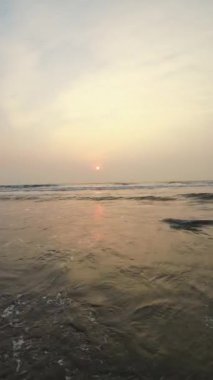 Kumsalda güzel sisli bir gün batımı. Dalgalar ve kara kumlarla.