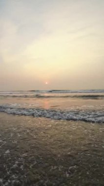 Kumsalda güzel sisli bir gün batımı. Dalgalar ve kara kumlarla.