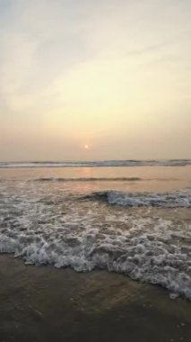 Kumsalda güzel sisli bir gün batımı. Dalgalar ve kara kumlarla.