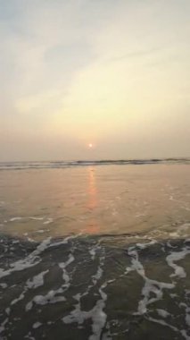 Kumsalda güzel sisli bir gün batımı. Dalgalar ve kara kumlarla.