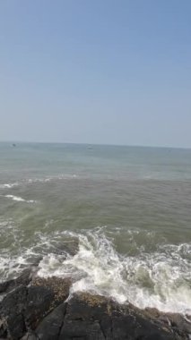 Okyanus dalgaları kıyıdaki büyük siyah kayalara çarpıyor.