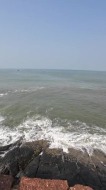 Okyanus dalgaları kıyıdaki büyük siyah kayalara çarpıyor.